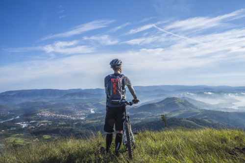 biker holding mountain bike on top of mountain with green grass